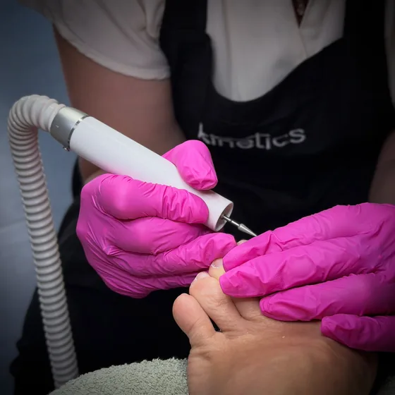 Fußpflege im Studio mit Fräser und pinken Handschuhen