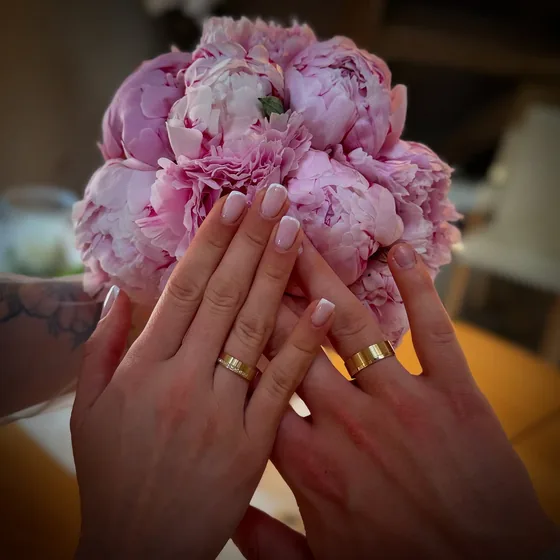Roséfarbene Nägel vor einem Strauß rosa Pfingstrosen