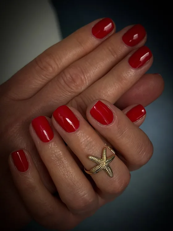 Glänzend rote Nägel an beiden Händen mit einem goldenen Sternring