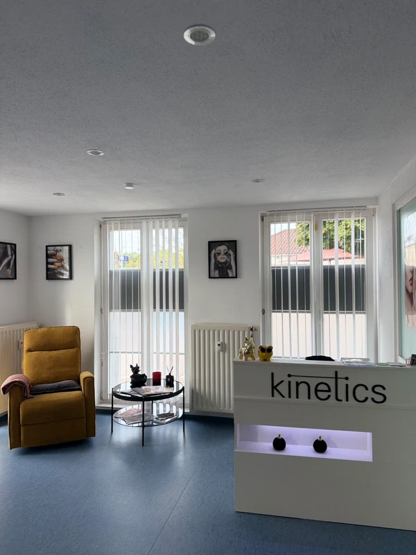 Empfangstresen mit Kinetics-Schriftzug, gelber Sessel und kleiner Tisch vor den Studiofenstern